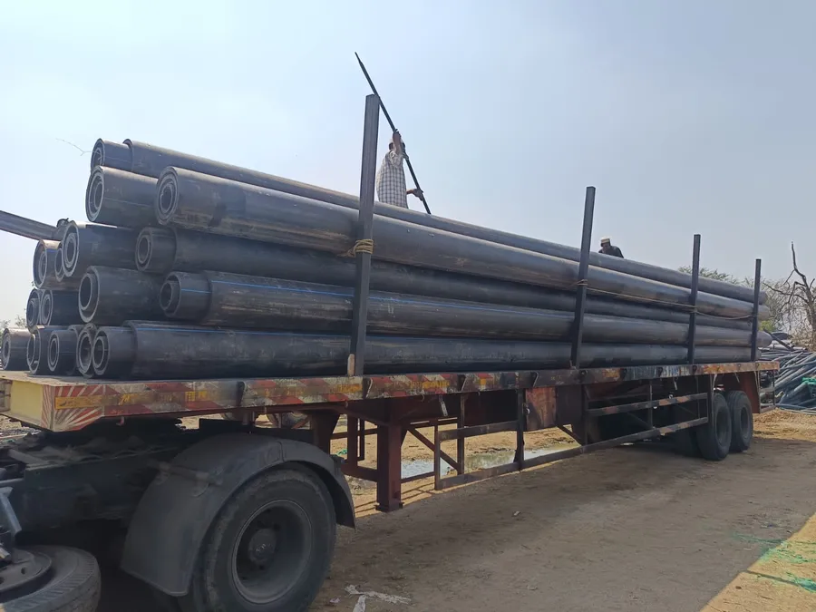 A flatbed trailer stacked with large black HDPE pipes under a blue sky