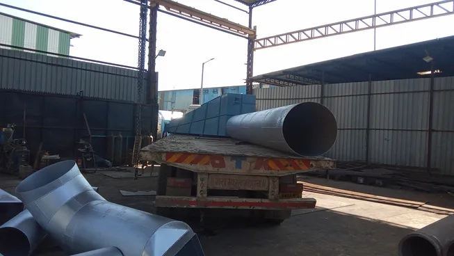 A very large steel pipe loaded on a truck inside a factory yard.