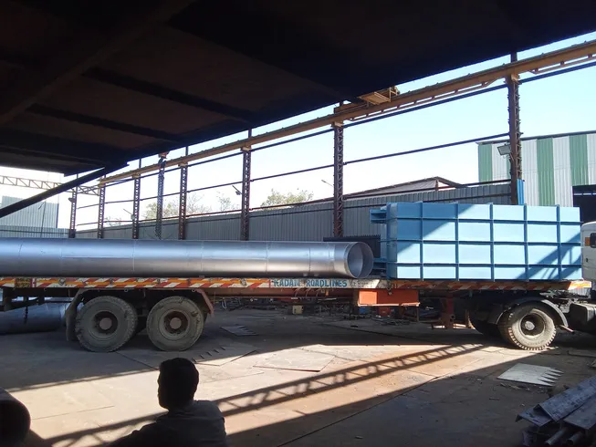 A galvanised pipe and a blue fabricated structure loaded on a truck under a factory shed
